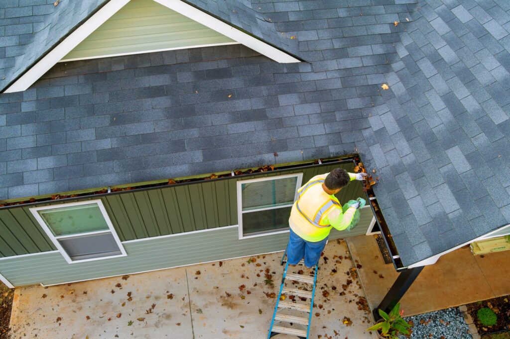 A worker is cleaning clogs in roof gutter drain by picking up dirt, debris, fallen leaves, replacement of gutters