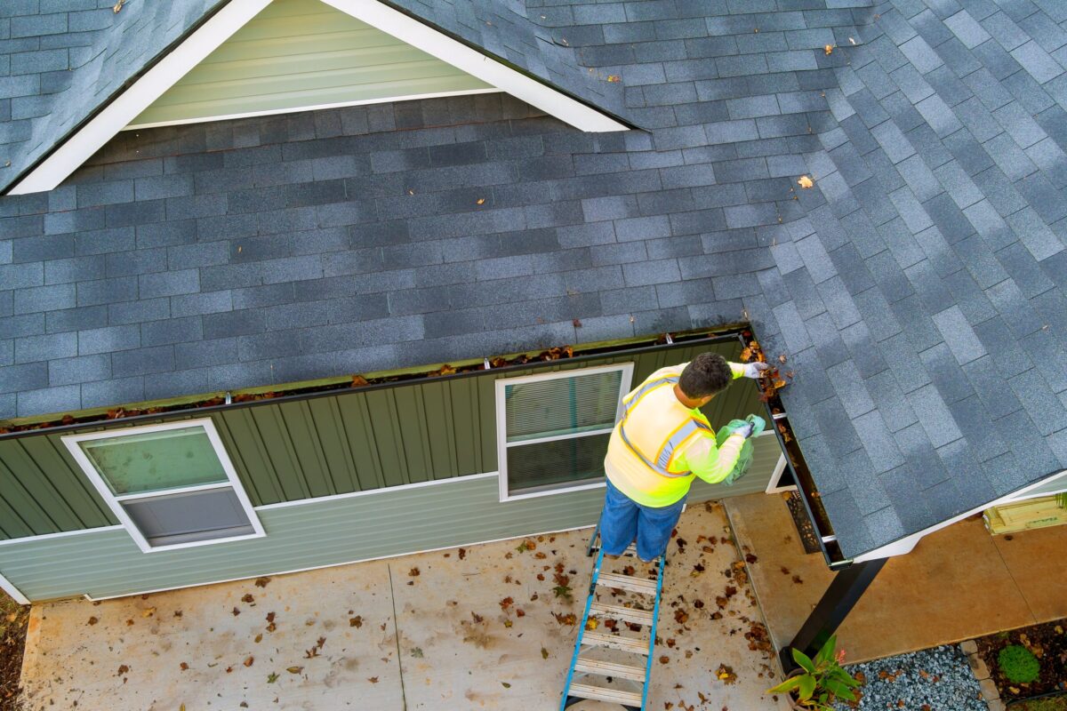 A worker is cleaning clogs in roof gutter drain by picking up dirt, debris, fallen leaves, replacement of gutters