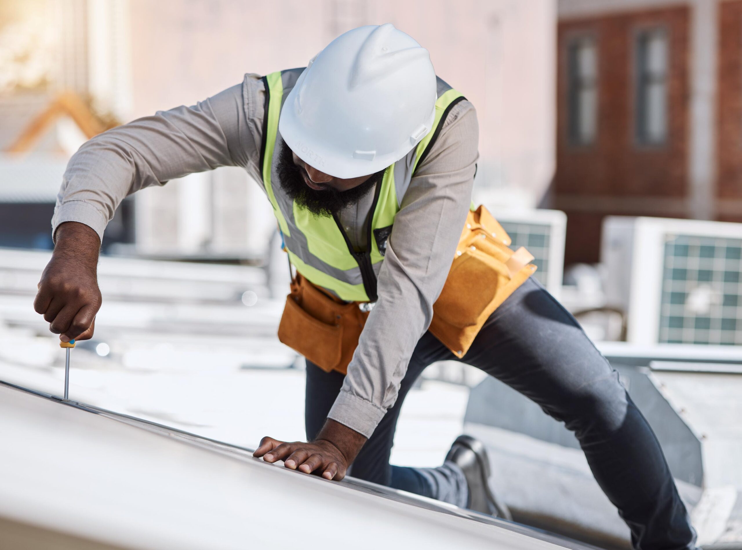 A roofer is shown kneeling and attaching a white panel to the roof of a building.