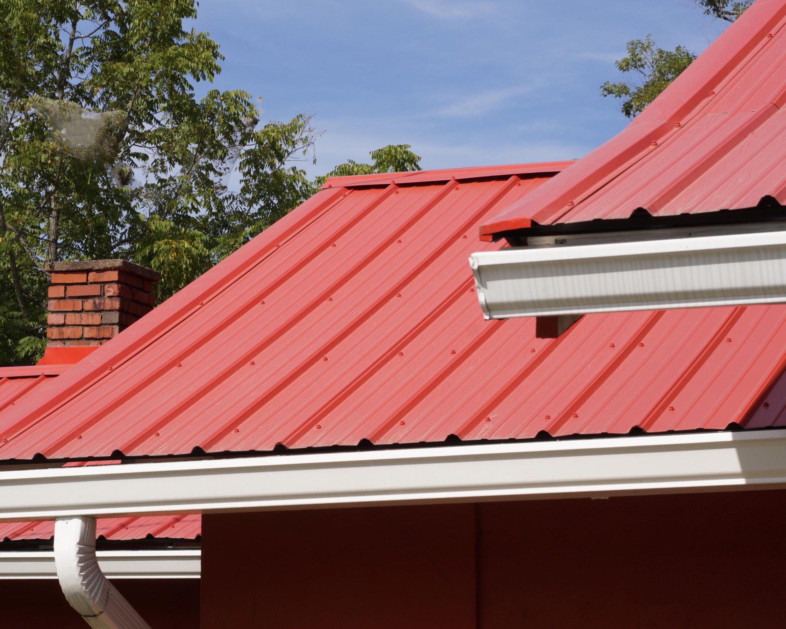 A lone figure with fair hair works on a metal roof with a tan building and windows below. This daytime shot focuses on construction and maintenance, evoking a mood of industry and craftsmanship.