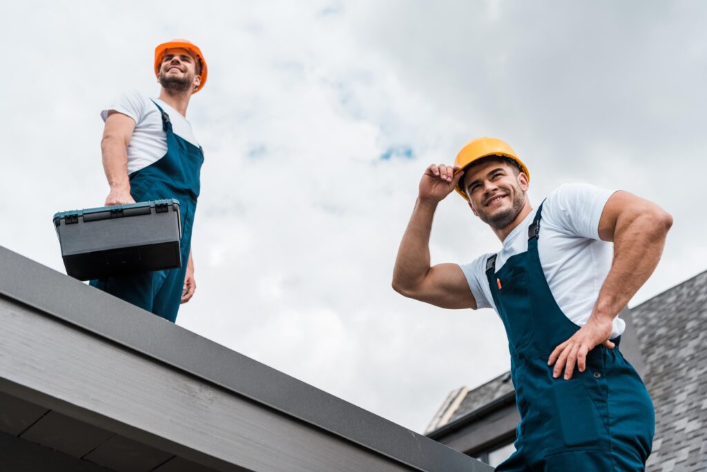 low angle view of happy handymen in helmets against sky with clouds
