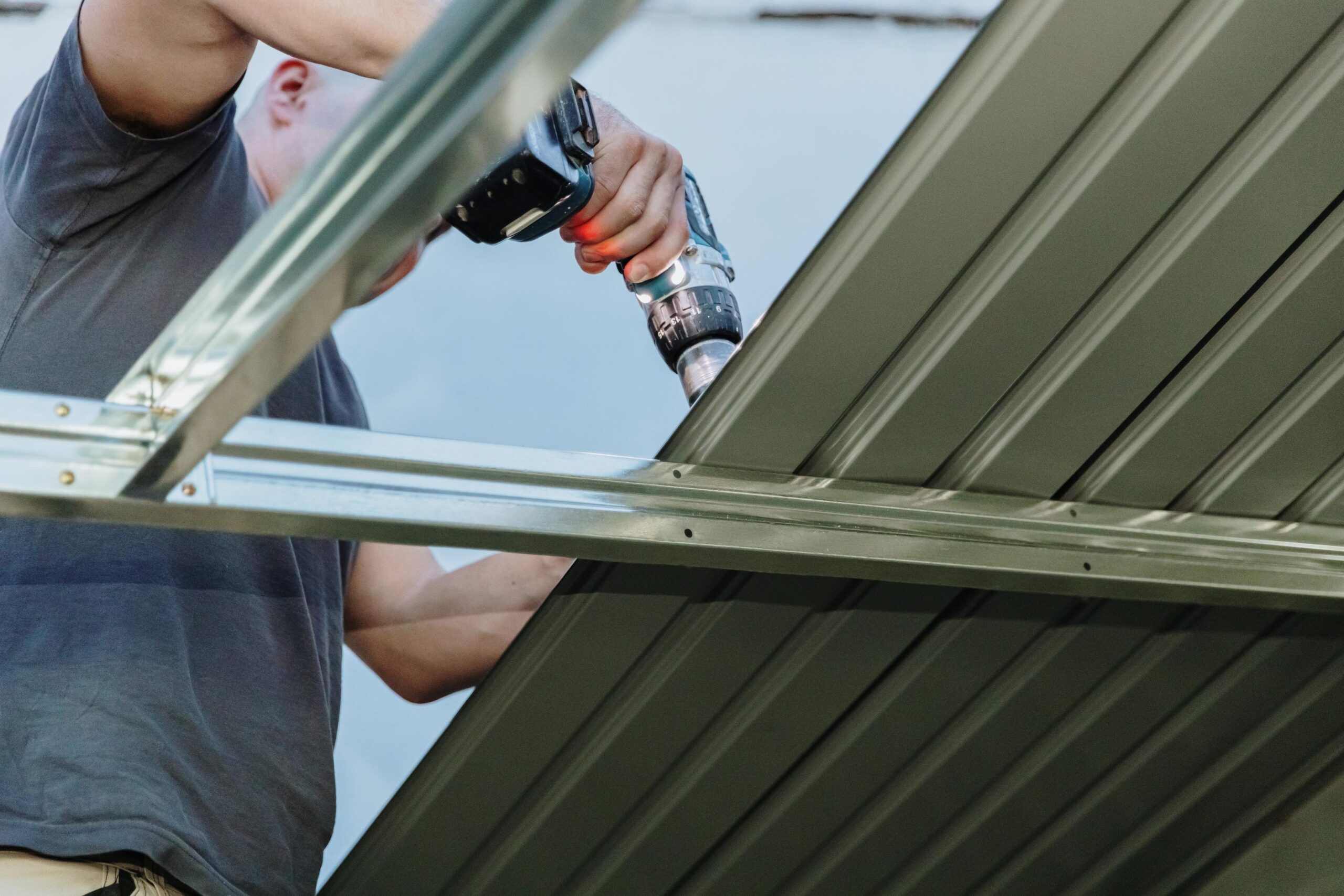 A mature roofer installs roofing sheets on a profile shed using a drill.