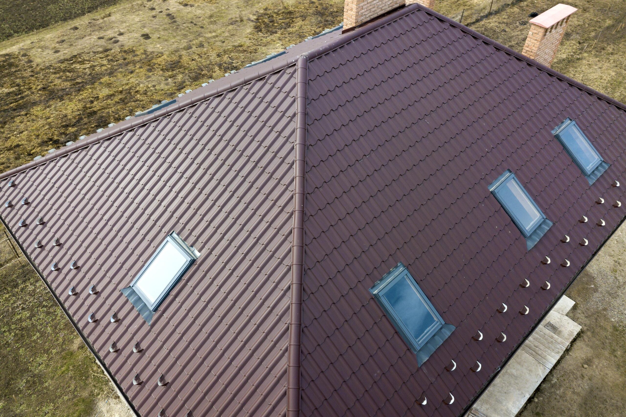 Aerial top view of building steep brown shingle roof, brick chimneys and small attic windows on house top with metal tile roof. Roofing, repair and renovation work.