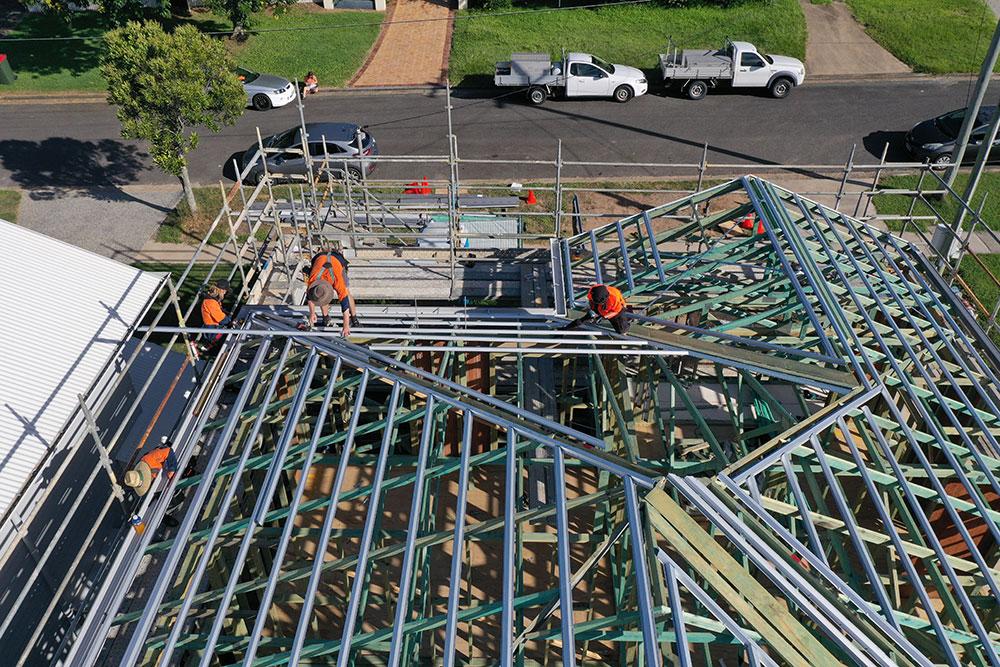 Workers install a steel roof frame on a building under construction, seen from above.
