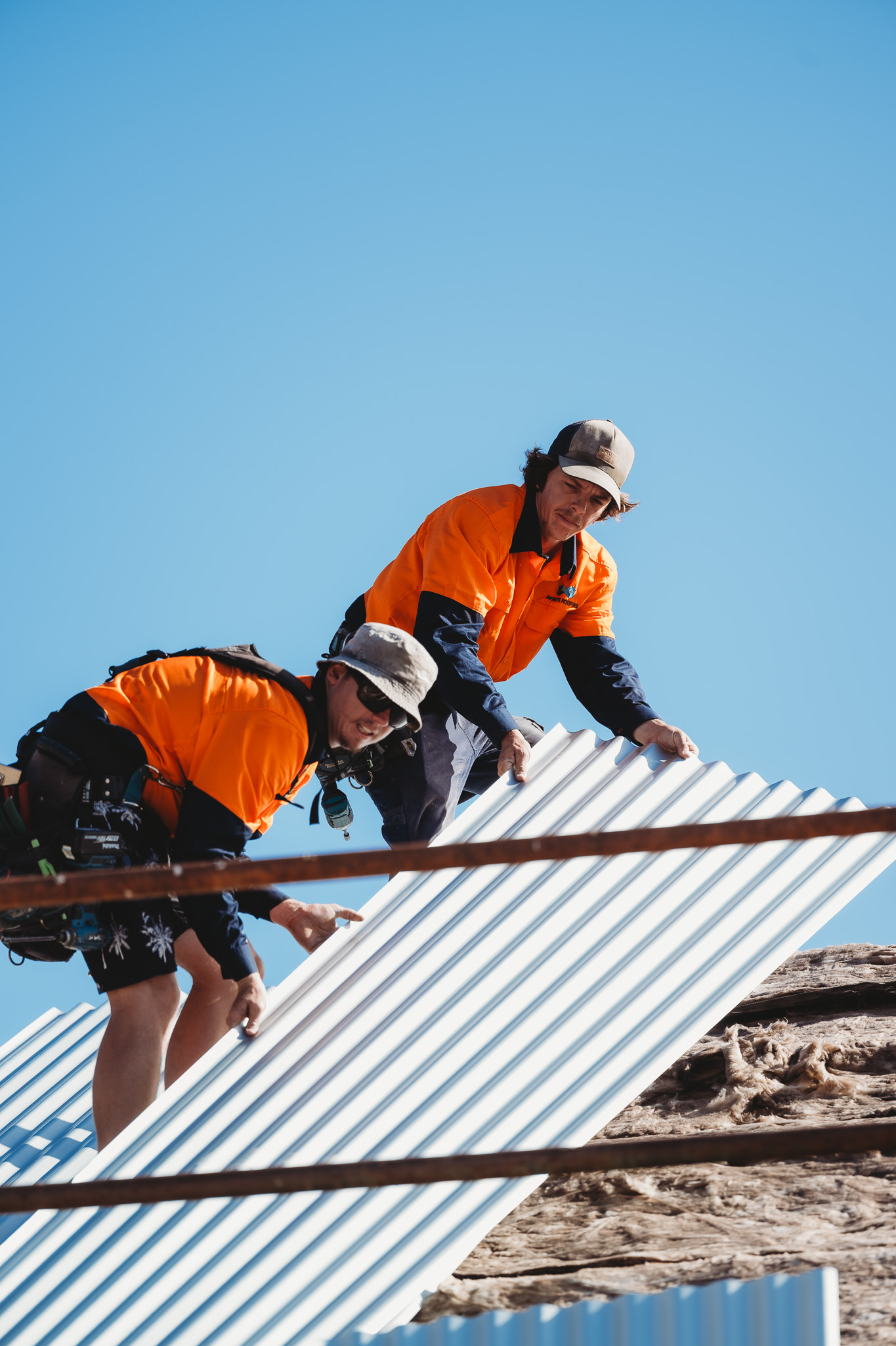 Two roofers lifting a corrugated metal roofing sheet into position