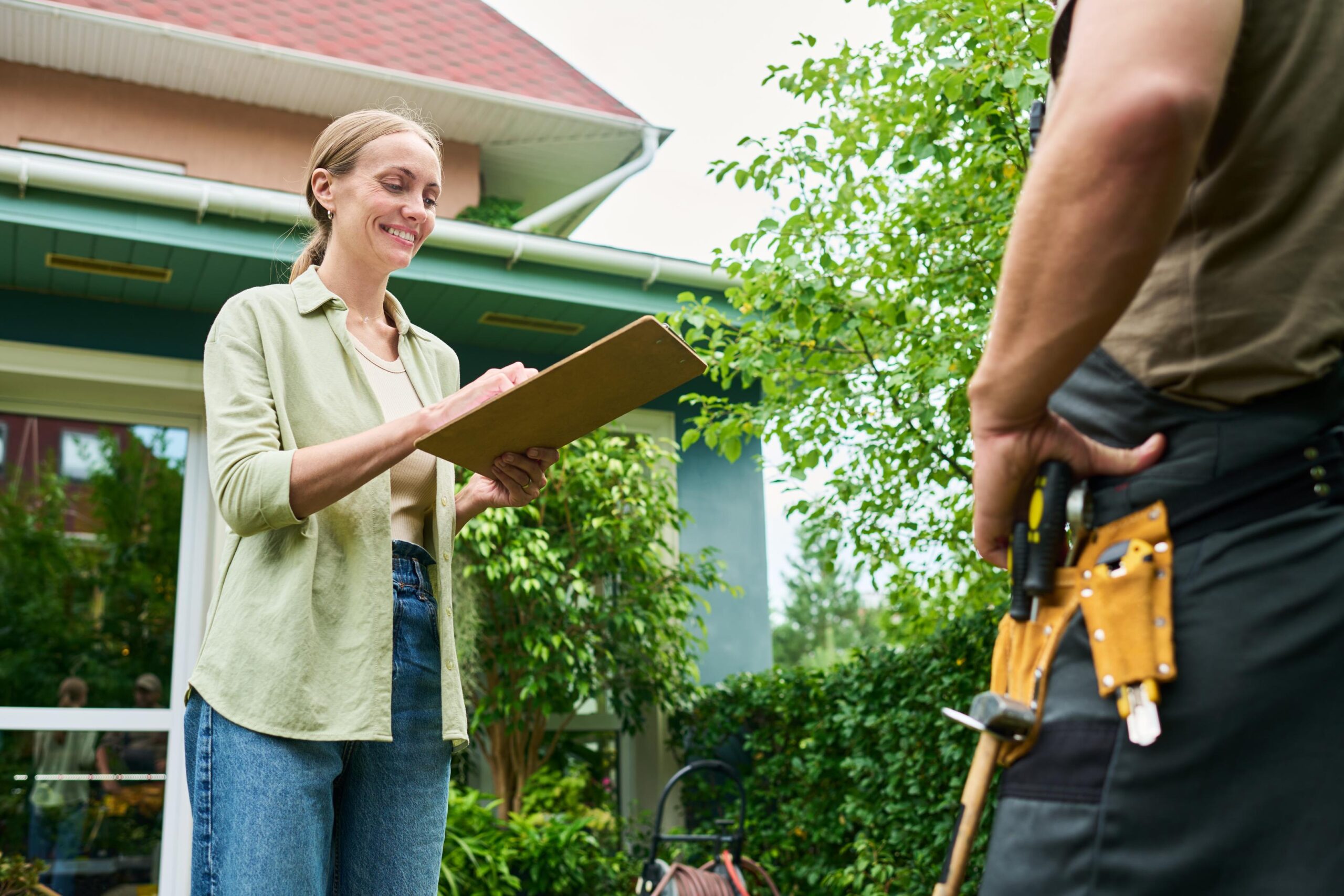 Woman Client Signing Documents on Clipboard with Contractor Outside House